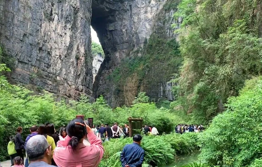 武隆の高い岩壁と自然の開口部の下にいる訪問者。
